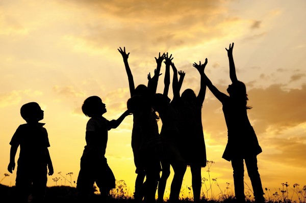 Group of children silhouettes playing on nature field at sunset